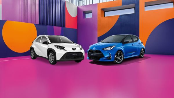 Ein weißer Toyota Aygo X und blauer Toyota Yaris stehen nebeneinander auf einen bunten Hintergrund.