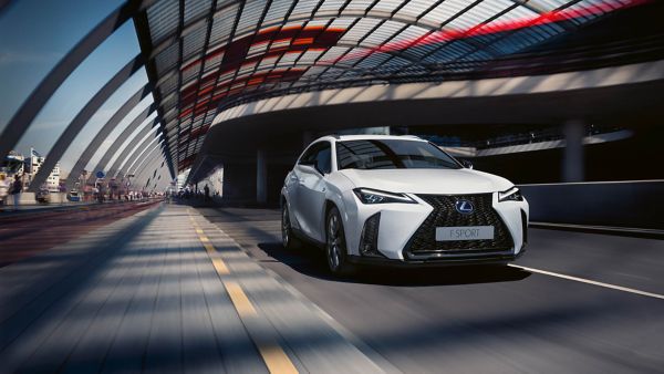 Un Lexus UX blanche circule dans une rue urbaine, mettant en valeur son design élégant et ses caractéristiques distinctives.