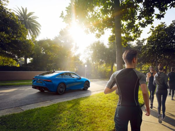 Mirai driving in the city with joggers in the foreground.