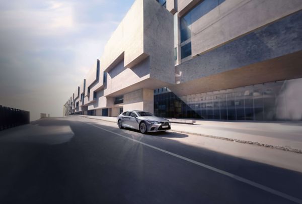 Eine elegante silberne Lexus LS Limousine fährt auf einer modernen Stadtstraße mit dramatischen architektonischen Strukturen im Hintergrund.