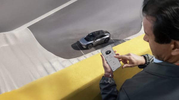 Ręka trzyma uniesiony smartfon z otwartą aplikacją TOYOTA MyT, wyświetlającą zakładkę 'Mój Garaż' z dostępnymi usługami połączonymi (Connected Services).