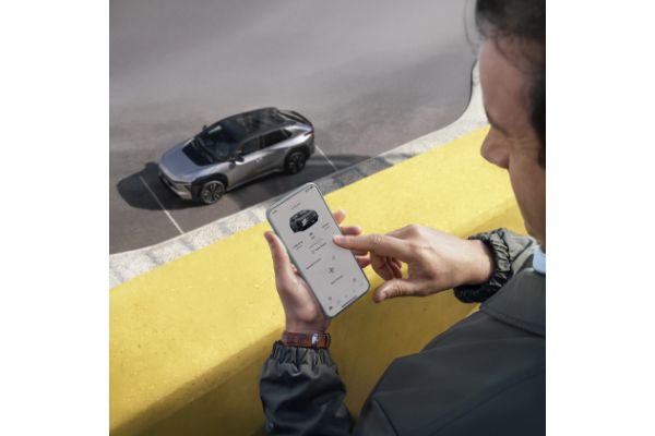 Ręka trzyma uniesiony smartfon z otwartą aplikacją TOYOTA MyT, wyświetlającą zakładkę 'Mój Garaż' z dostępnymi usługami połączonymi (Connected Services).