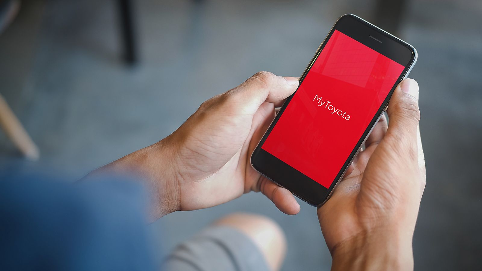 Een passagier zit in de bestuurderstoel van een Toyota, met zijn smartphone in zijn hand. Het didplay toont het logo van de TOYOTA MyT app.