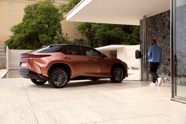 Eine Person geht auf einen vor einem Haus geparkten Lexus RZ zu, der an einer Wallbox lädt