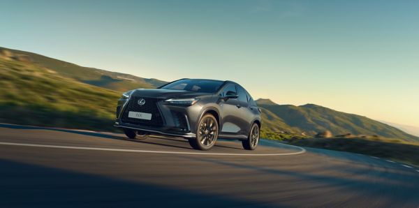 Ein schwarzer Lexus NX fährt auf einer kurvigen Bergstraße bei klarem Himmel, umgeben von grünen Hügeln im Hintergrund.