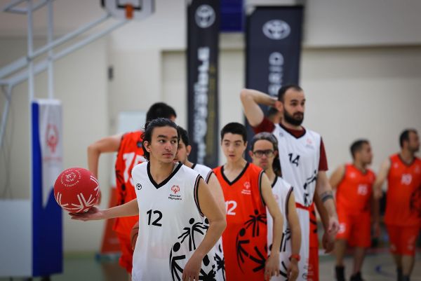 Elinde basketbol topu tutan bir sporcu ve arkasında sporcular