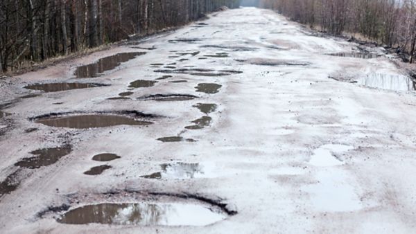 geteerte Straße mit vielzähligen Schlaglöchern, in denen sich Regenwasser gesammelt hat