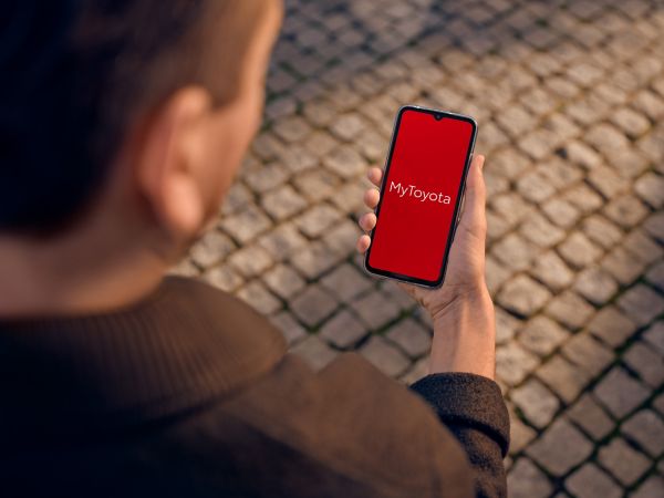 Person hält ein Smartphone in der Hand, auf dem ein roter Bildschirm und ein MyToyota Schriftzu zu erkennen ist