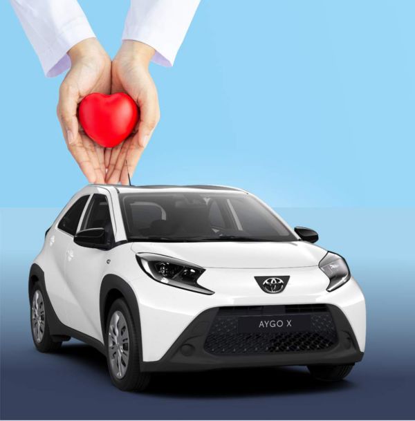 Weißer Toyota Aygo X auf blauem Hintergrund, darüber zwei Hände, die ein rotes Herz halten – Symbol für Fürsorge und emotionale Verbindung zum Fahrzeug.