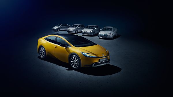 Mehrere graue Prius Modelle auf dunklem Hintergrund mit einem gelben Prius Plug-In Hybrid im Vordergrund.