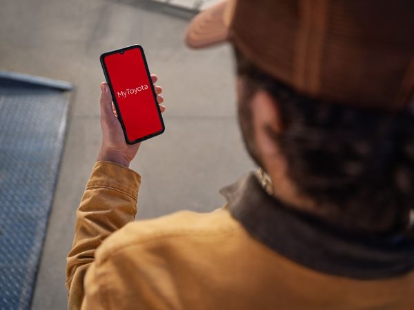 Eine Person hält ein Smartphone mit der „myToyota“-App auf einem leuchtend roten Hintergrund