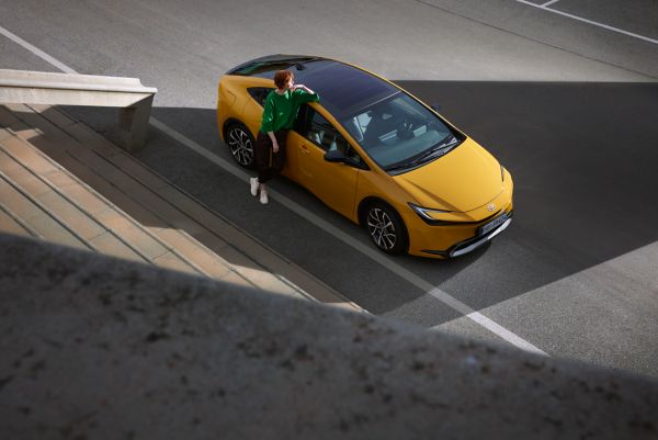 Gelber Toyota Plug-in Hybrid steht am Straßenrand und eine Person lehnt an der Wagentür.