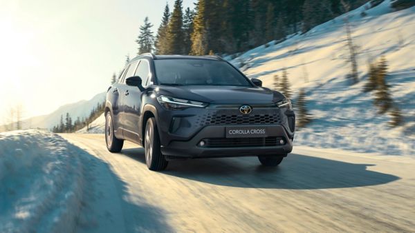 Der Toyota Corolla Cross fährt sicher und stabil auf einer verschneiten Straße, umgeben von winterlicher Landschaft. 