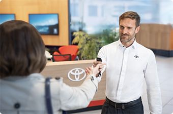 Pracownik w salonie Toyoty przekazuje kluczyk klientce.