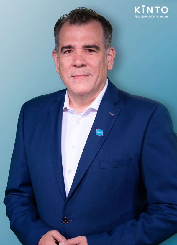 Christian Gelhard trägt ein Sakko mit dem Kinto-Logo und steht vor einem Hintergrund mit dem Markenzeichen: Kinto