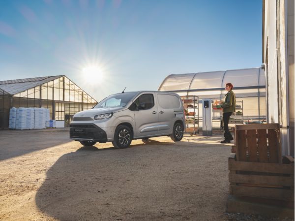 Toyota Proace City Electric vor Gewächshäusern bei Sonnenaufgang, daneben eine Person mit Kiste.