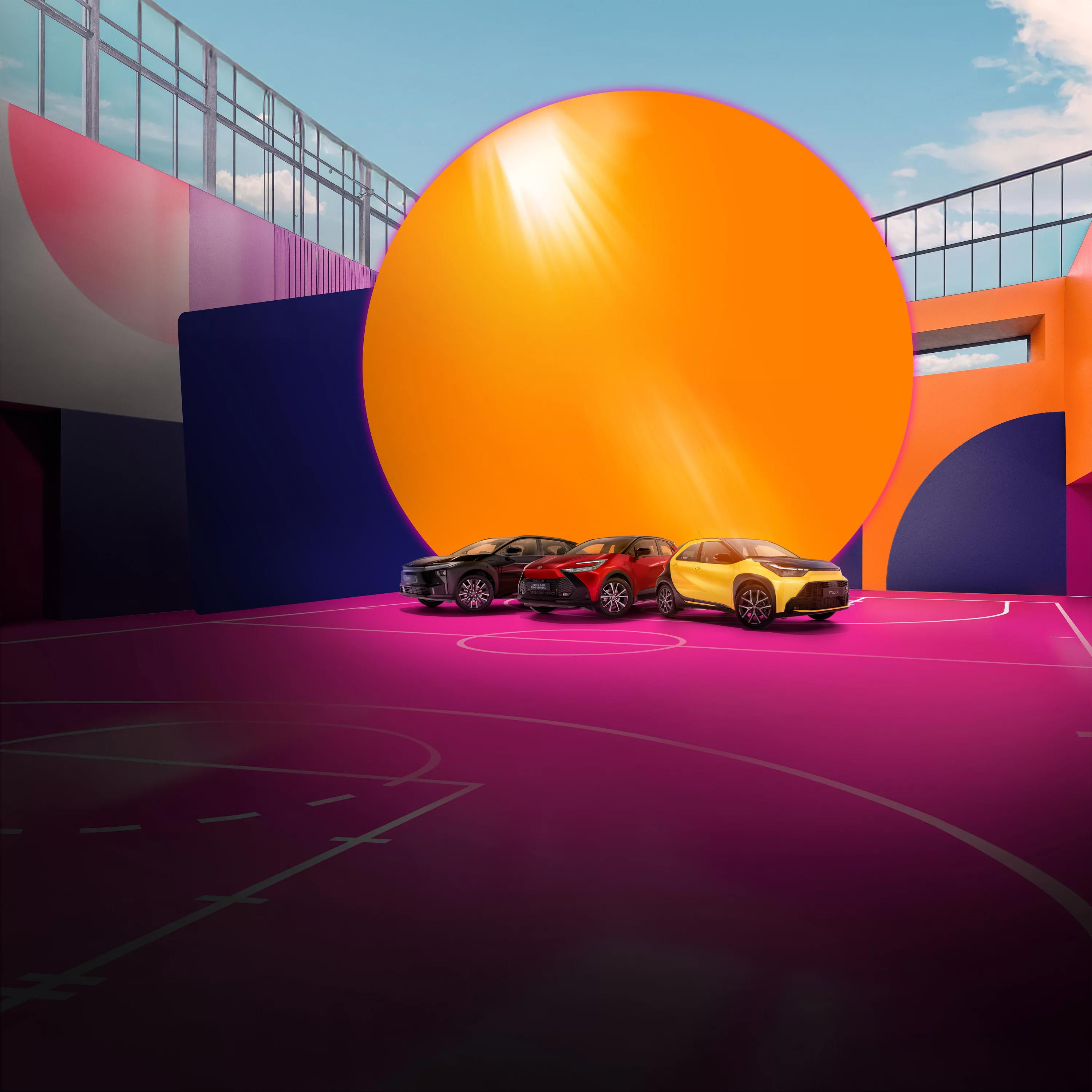 Vier Toyotas stehen auf einem pinken Basketballplatz, der von einer bunt bemalten Wand umgeben ist.