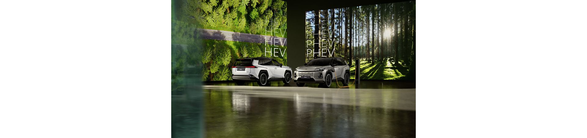 Studio set: a silver Toyota RAV4 PHEV charging, a white RAV4 Hybrid parked beside it. Forest scenes shown on two large background screens.