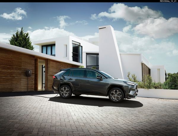 Ein grauer RAV4 Plug-in steht in der Einfahrt eines modernen Hauses und lädt über eine Wallbox.