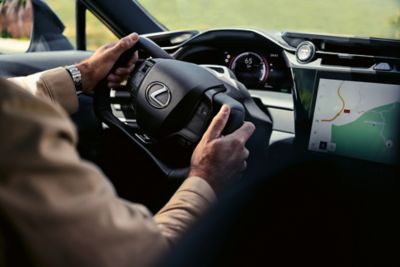 Innenansicht eines Lexus RZ, die das Lenkrad, das Touchscreen-Display und das moderne Design des Armaturenbretts vor einer malerischen Kulisse zeigt.