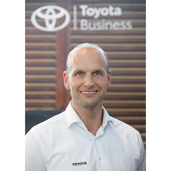 Ronny Schlärmann trägt ein Hemd mit dem Toyota-Logo und steht vor einem Hintergrund mit dem Markenzeichen: Toyota Business