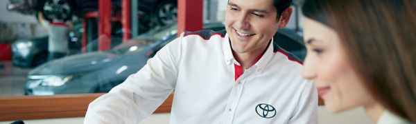 Servis alanında aynı yere bakarak gülümseyen bir Toyota çalışanı ile gülümseyen bir kadın