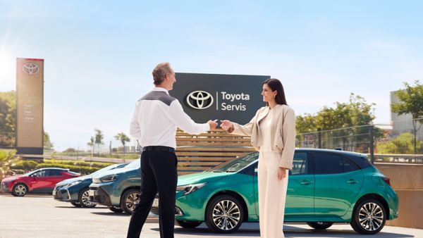 arka planda çeşitli Toyota marka araçlar olan bir Toyota servis noktasında müşteri ve servis çalışanının araç anahtarını teslim alıp verirken el sıkışması 