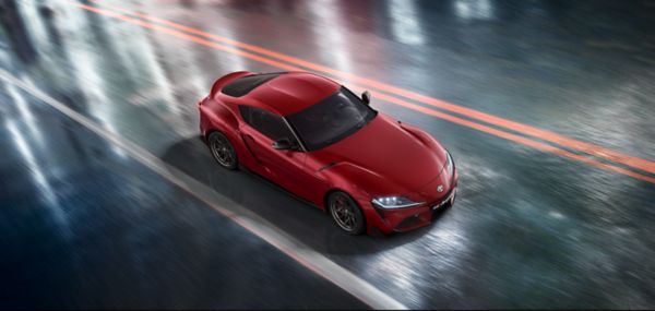 Sicht auf einen roten Toyota GR Supra von schräg oben, der auf einer nassen Fahrban fährt