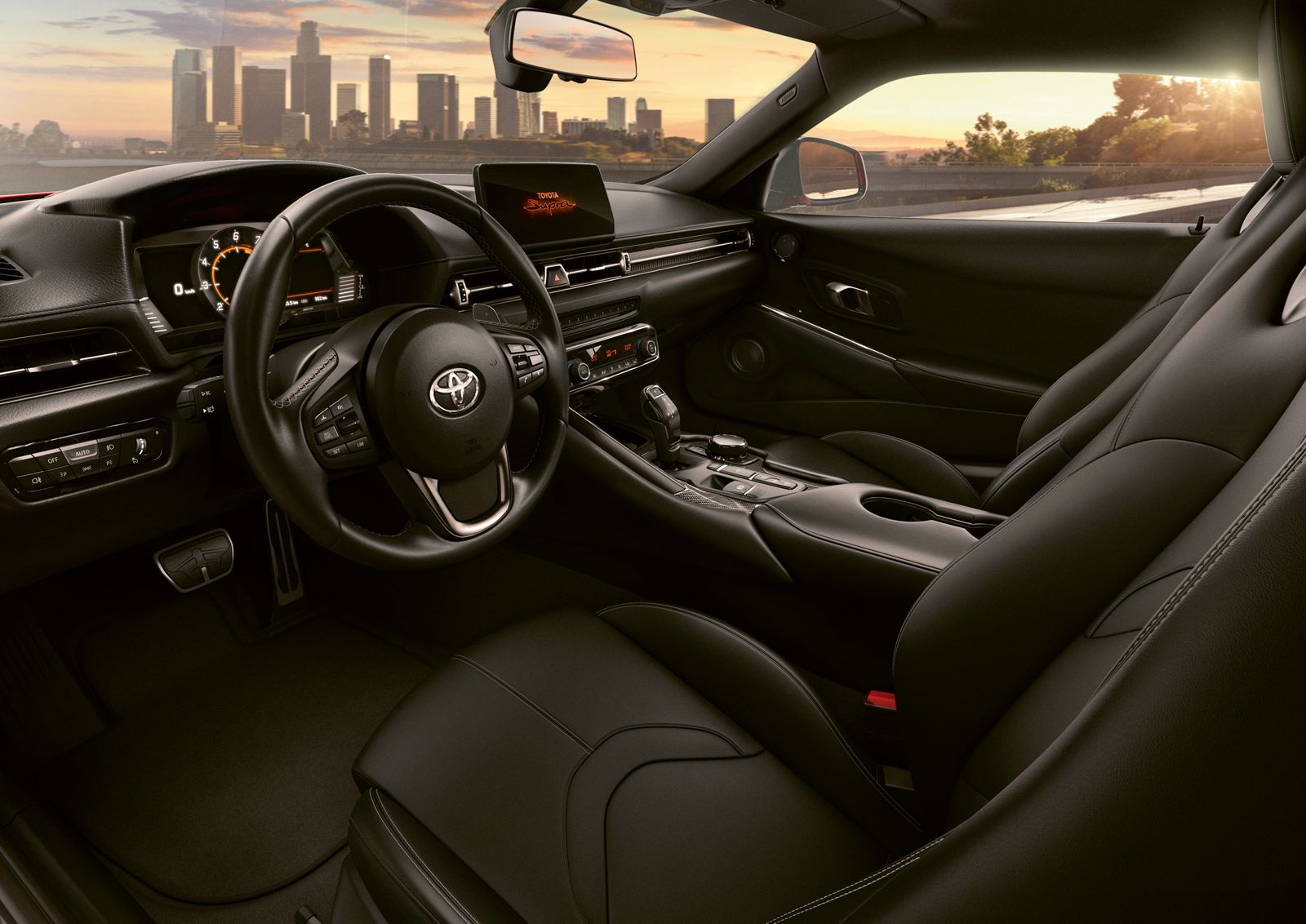 Blick auf das Cockpit und die Vordersitze des GR Supra , im Hintergrund die Skyline einer Stadt im Sonnenuntergang.