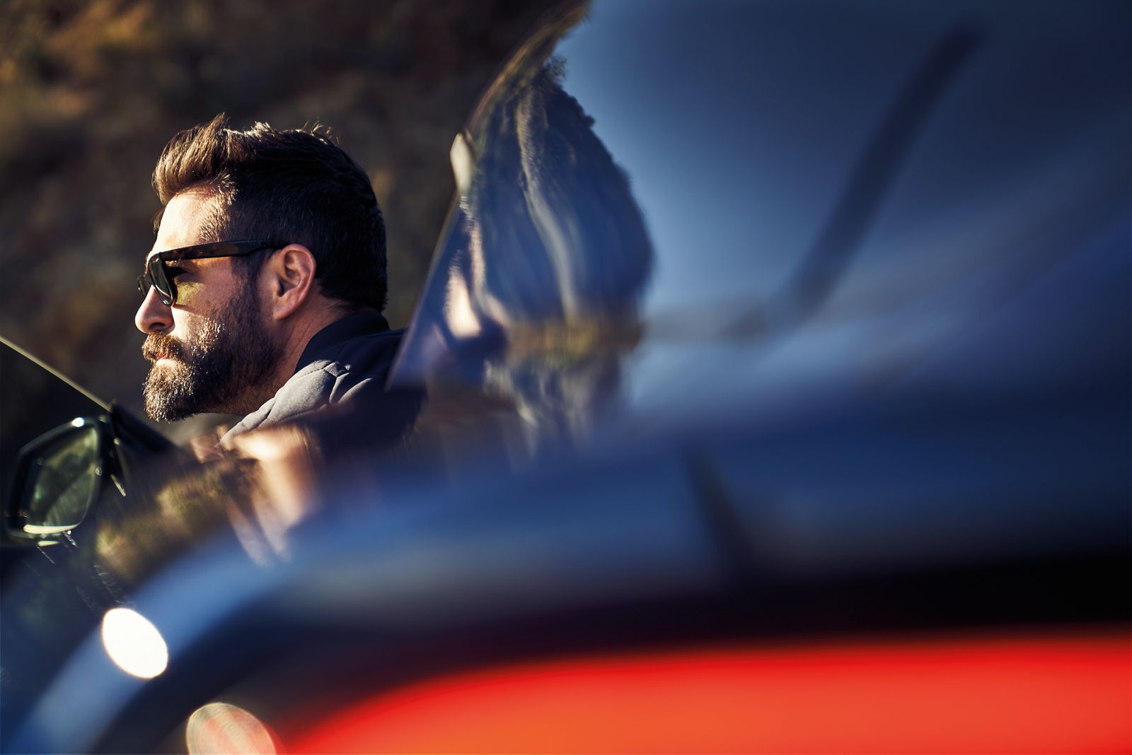 Kopf eines Mannes mit Sonnenbrille, der aus einem dunklen GR Supra steigt, Fahrzeug unscharf aber prominent im Vordergrund mit leuchtenden Rücklichtern.