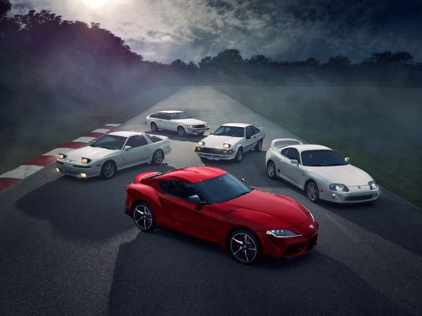 Mehrere Generationen des Toyota Supras stehen hintereinandergereiht auf einer Rennstrecke. Es ist dunkel und ein Nebelschleier liegt über der Straße.