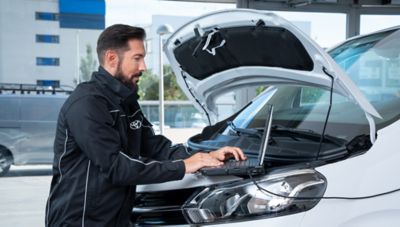 Ein Toyota-Servicetechniker führt unter geöffneter Motorhaube mit einem Laptop eine Fahrzeugdiagnose durch