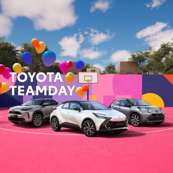 Toyota C-HR in der Mitte, linke Yaris Cross und rechts Aygo X auf einem bunten Basketballfeld. In der Mitte hinter den Modellen ein Basketballkorb, Blauer Himmel mit wenigen weißen Wolken. Luftballons links, die in die Luft steigen und ein Toyota Teamday Schriftzug links über dem Yaris Cross schwebend.