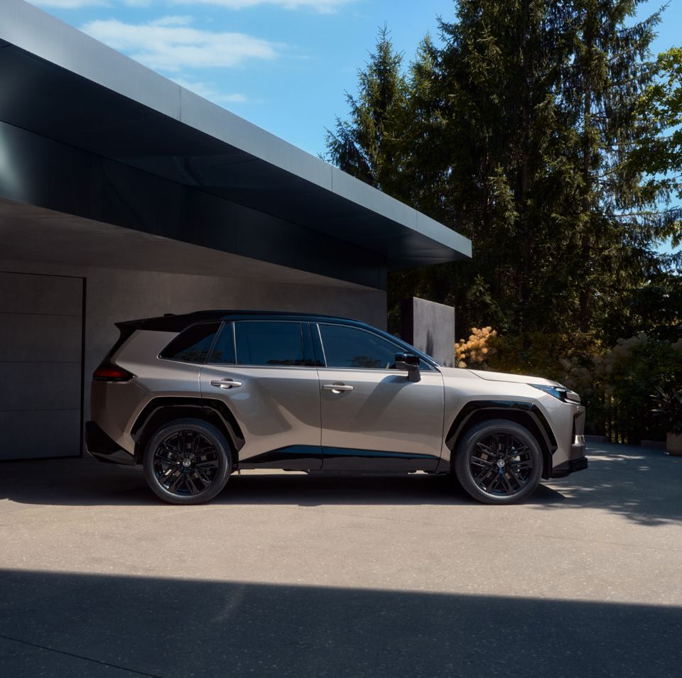 Toyota RAV4 stoi zaparkowana przed nowoczesnym domem jednorodzinnym, w tle drzewa