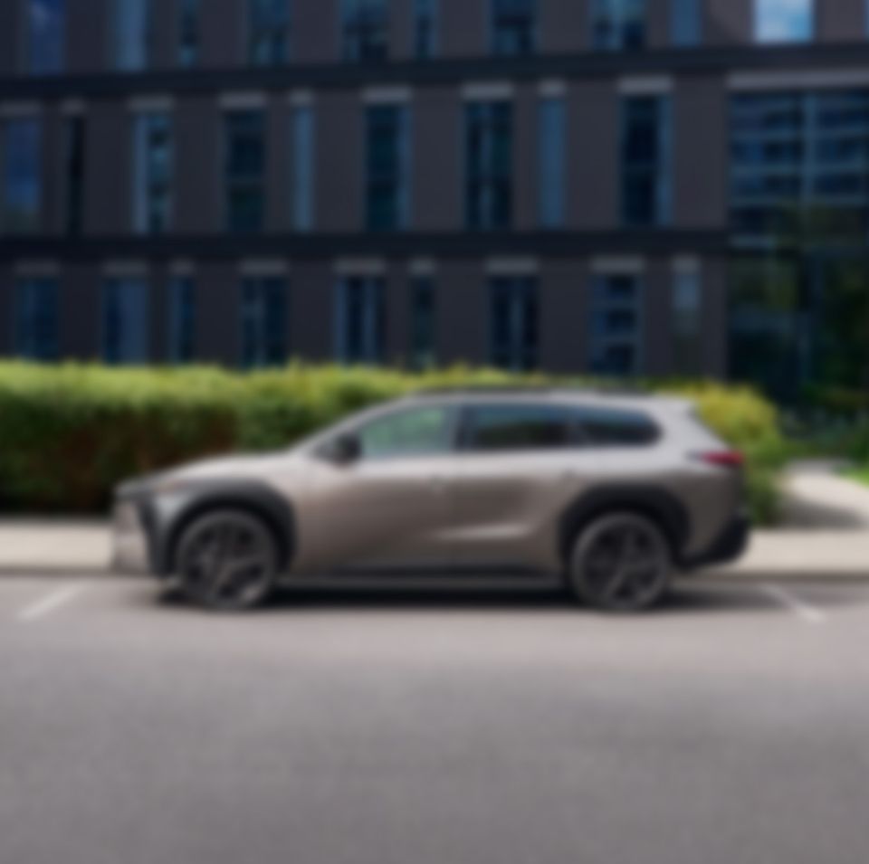 Zamglone zdjęcie Toyoty BZ4X Touring na tle żywopłotu i wysokiego budynku