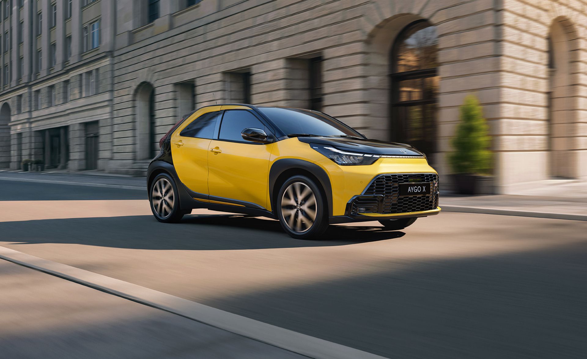 Żółta Toyota Aygo X na tle monumentalnego budynku