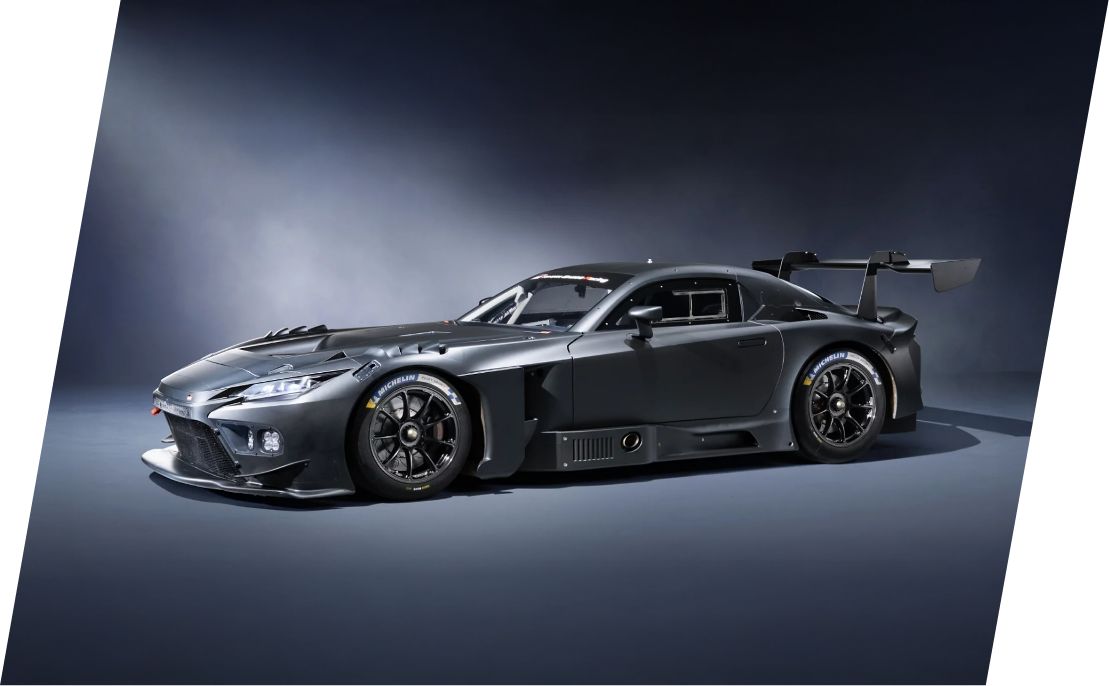 Egy sötétkék Toyota Gazoo Racing versenyautó, fehér és piros mintákkal, kivilágított fényszórókkal, egy garázsban állva.