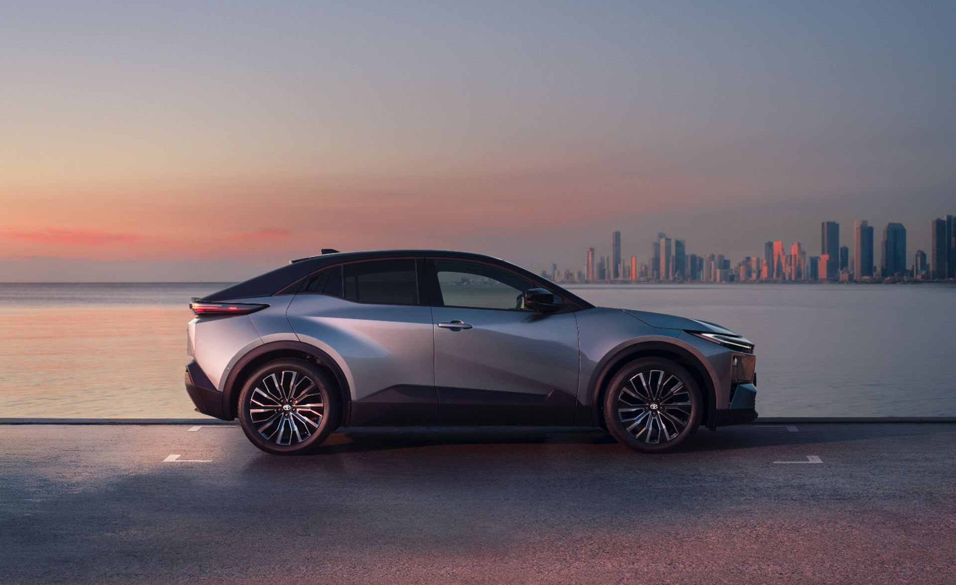 Toyota C-HR a város látképével a víz túloldalán, naplementében