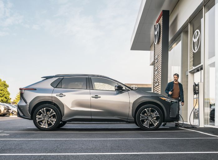 Mężczyzna podłącza Toyotę bZ4X do ładowania przy salonie Toyoty