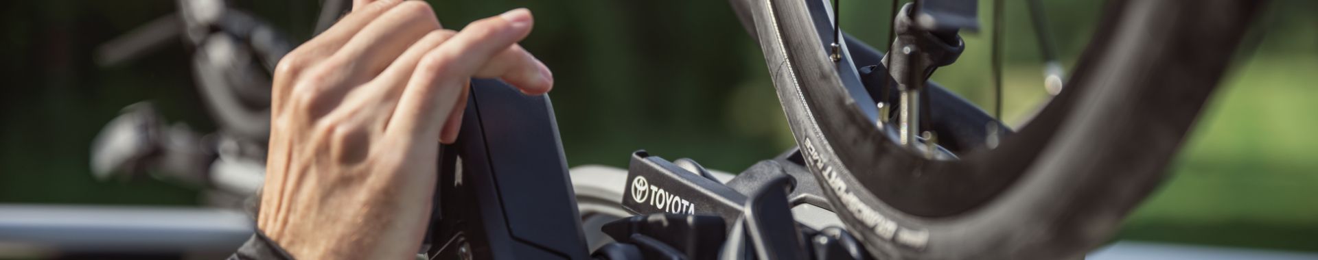 Ruka upevňuje jízdní kolo na nosič Toyota na zadní části vozidla.