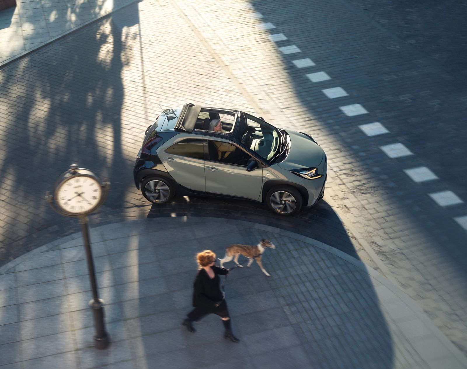 Aygo X drives sunny city streets with its canvas roof open. 