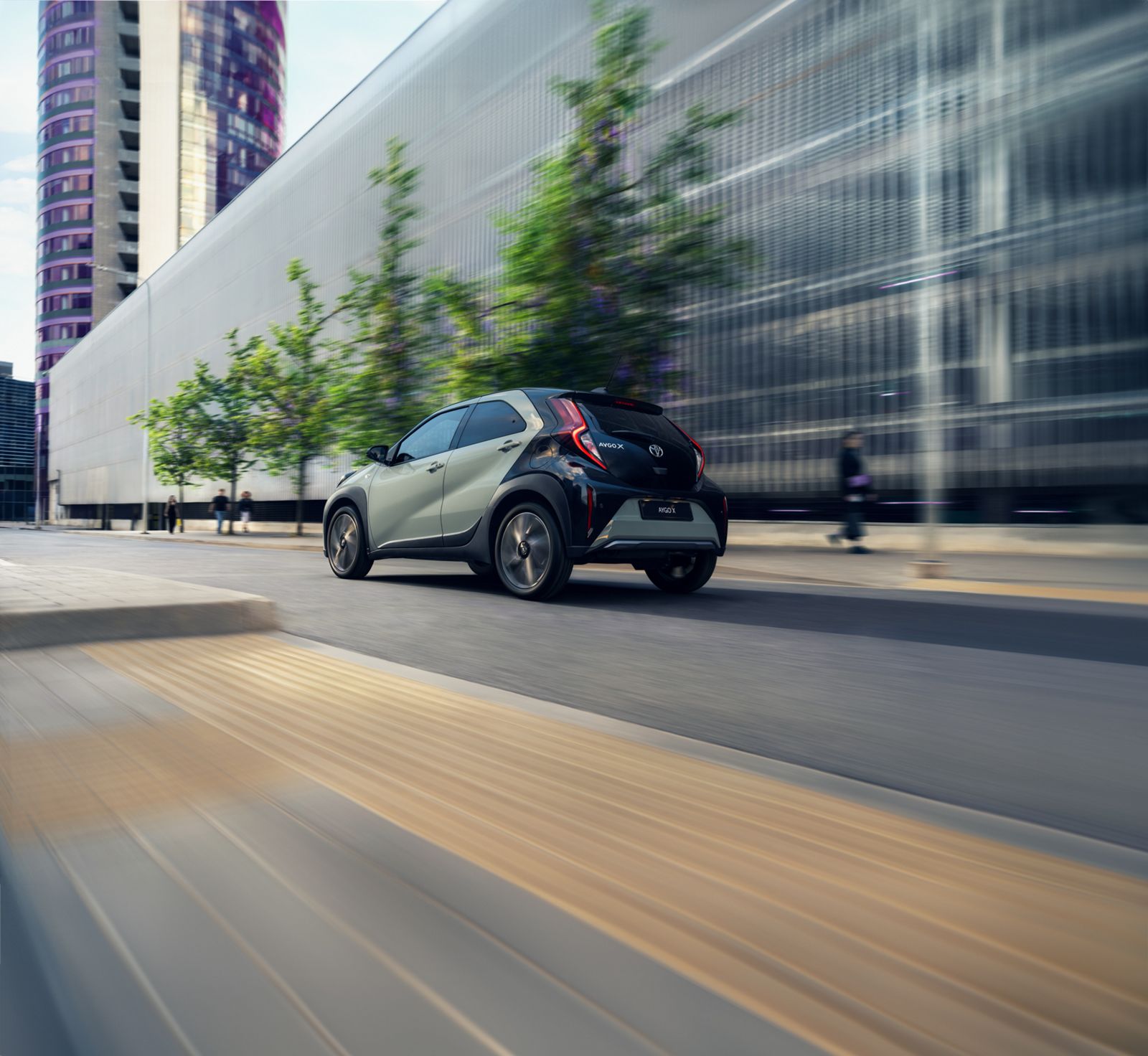 A Toyota Aygo X drives along a tree-lined boulevard.
