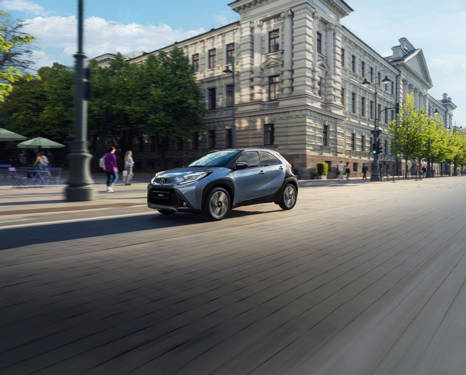 An Aygo X cruises along sun-dappled city streets 