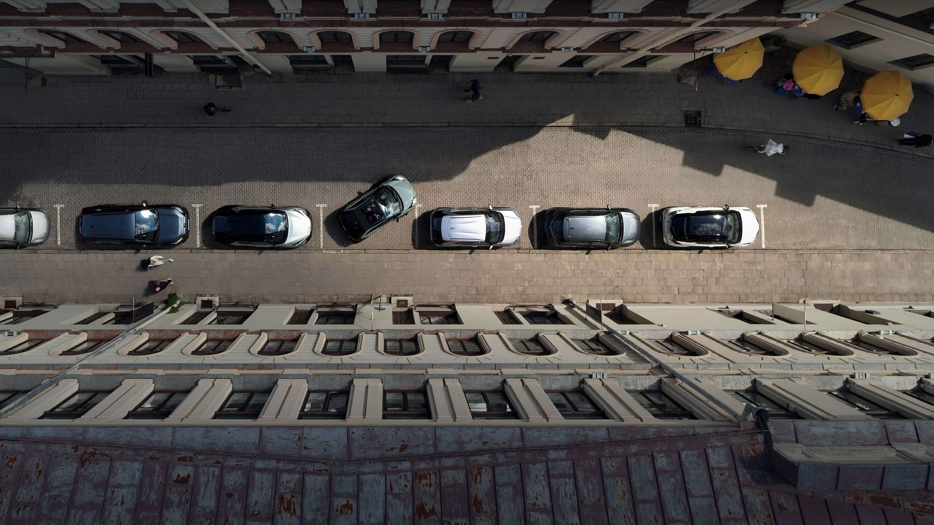 Vogelperspektive auf eine Straße mit parkenden Autos zwischen Wohnhäusern. Ein Aygo X parkt rückwärts in eine freie Lücke ein.