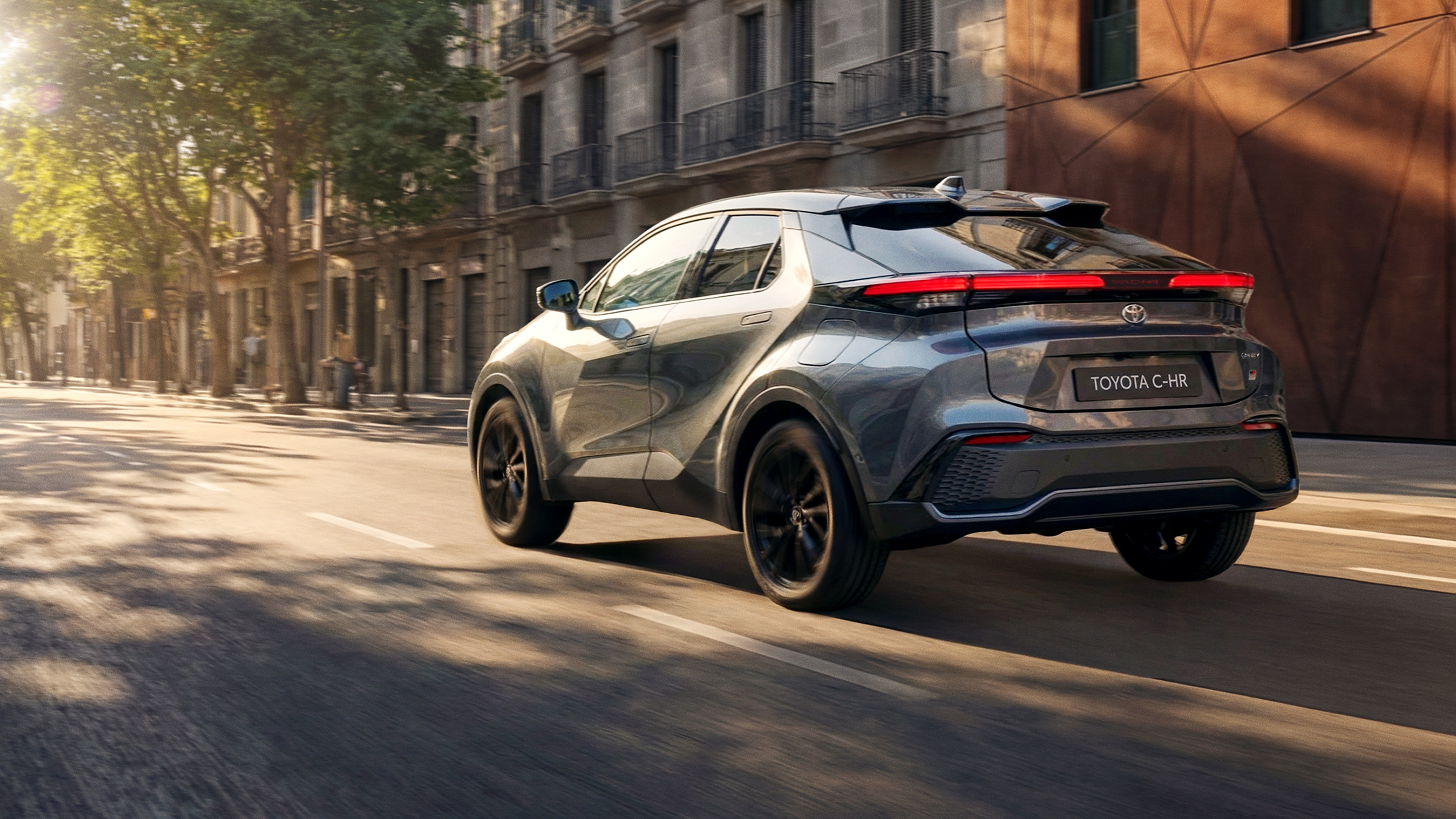 Ein Toyota C-HR fährt durch eine sonnige Stadtstraße mit moderner urbaner Architektur.