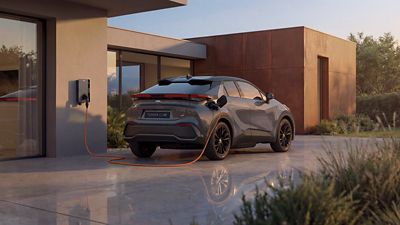 Ein Toyota C-HR lädt an einer Wallbox vor einem modernen Wohnhaus in zeitgemäßer Architektur.