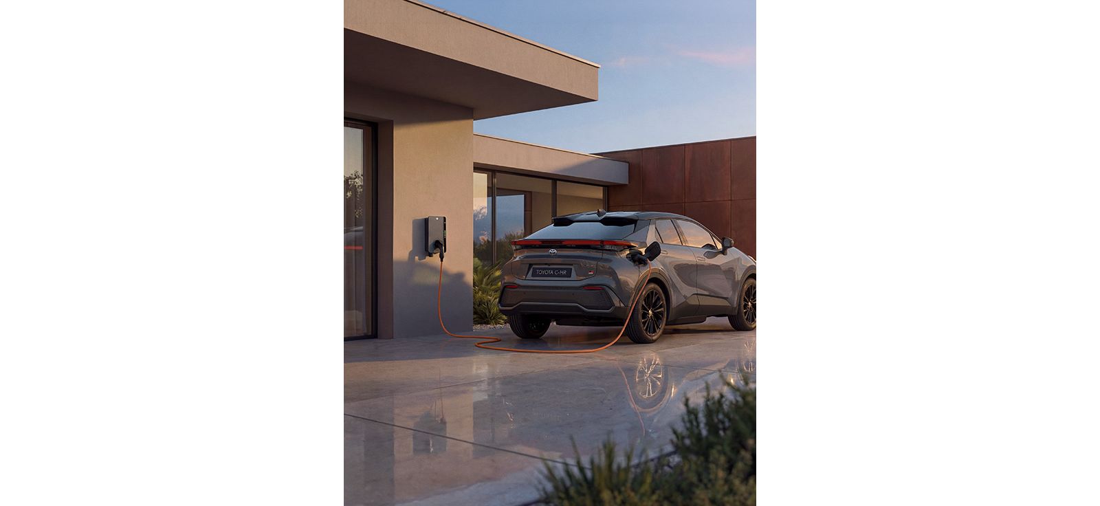 Ein Toyota C-HR lädt an einer Wallbox vor einem modernen Wohnhaus mit zeitgemäßer Architektur.