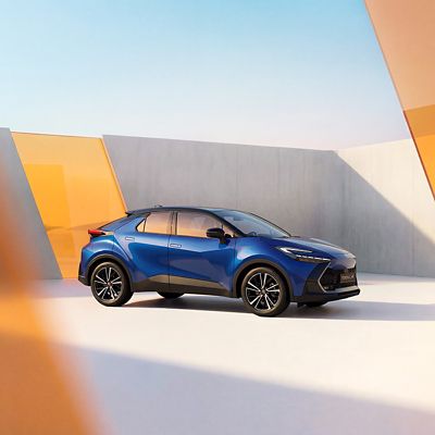 Blauer Toyota C-HR steht seitlich vor einer modernen, geometrischen Wand mit gelben und grauen Flächen unter klarem Himmel