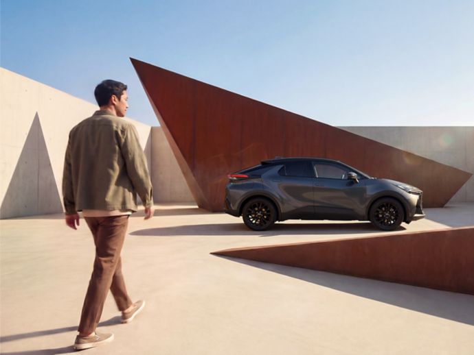 Ein Toyota C-HR steht vor moderner Architektur, während eine Person auf das Fahrzeug zugeht.