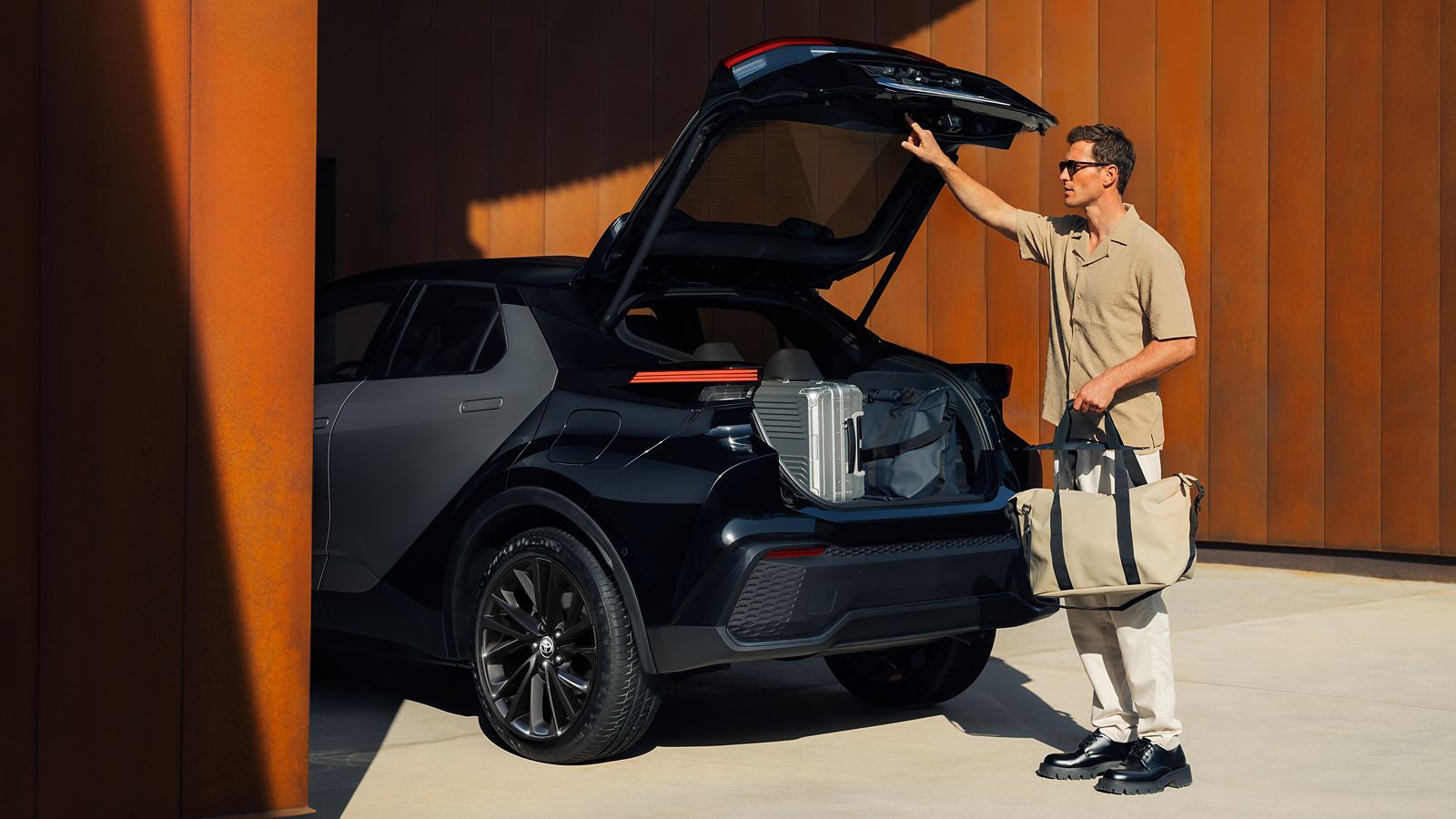 İçinde valizler olan Toyota C-HR Hybrid bagajını kapatan bir adam